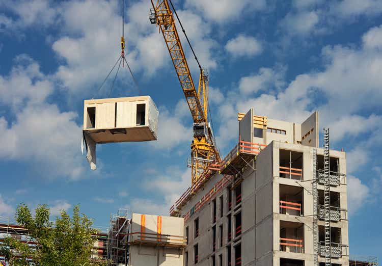 Crane lifting a wooden building module to its position in the structure.