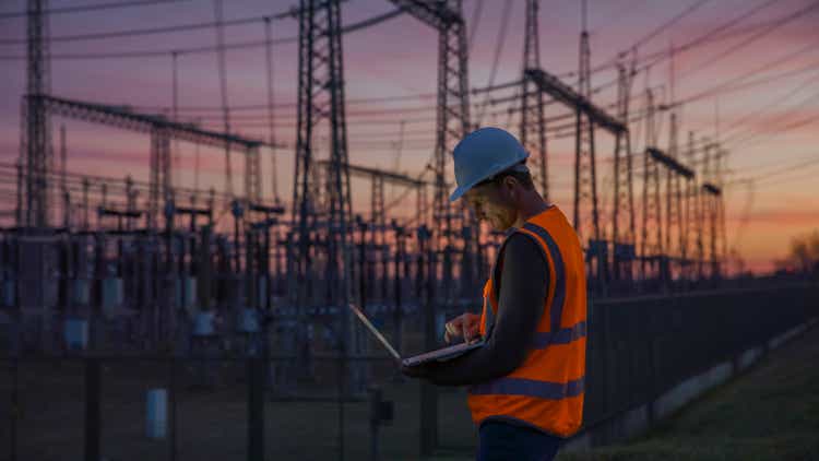 Confident male engineer using a laptop in front of electric power station