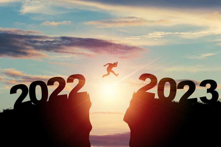 Welcome merry Christmas and happy new year in 2023,Silhouette Man jumping from 2022 cliff to 2023 cliff with cloud sky and sunlight.