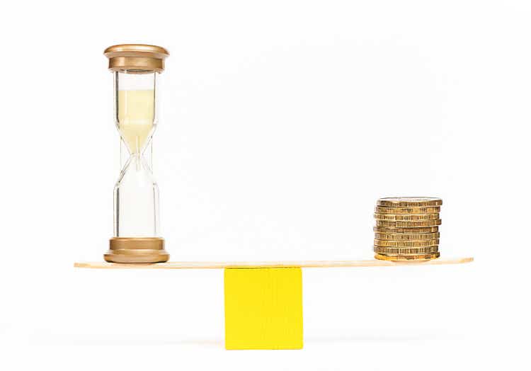 scales with hourglass and coins on white background