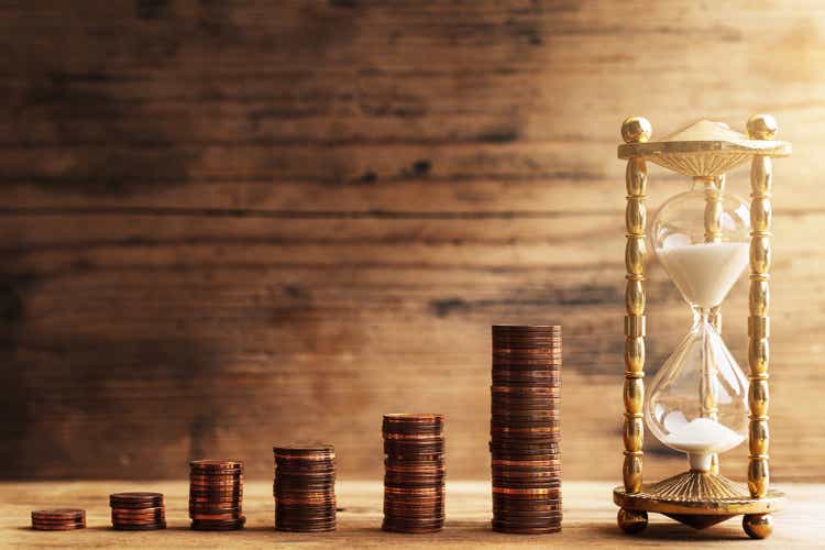 Hourglass with pouring sand and stacks of shiny small value copper euro coins.