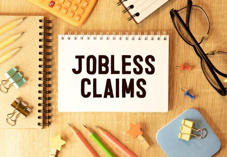 Jobless claims text on white paper from a notepad on a wooden background. wooden blocks magnifier.