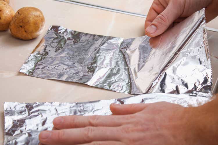 A man tears off the foil from plastic dispenser to wrap potatoes in it and bake them in the oven.