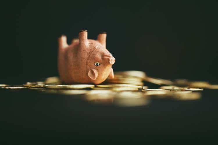Cute pink pig upside down on a pile of gold coins. Rolling in dough or money