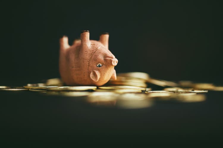 Cute pink pig upside down on a pile of gold coins. Rolling in dough or money