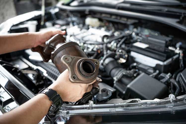 Close up old catalytic converter in hand Car service man remove from engine gasoline car dust clogged condition on filter in service concept and engine room in the background