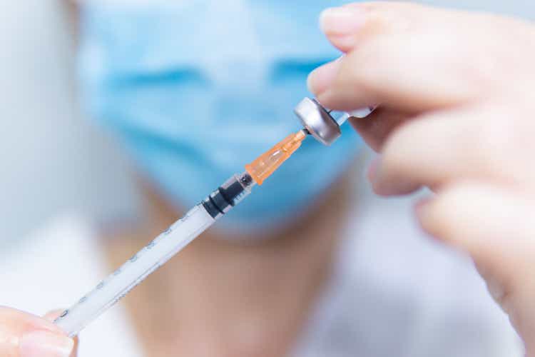 Close up of an unrecognizable nurse with face mask filling syringe with medication of a vial, health care and vaccination concept