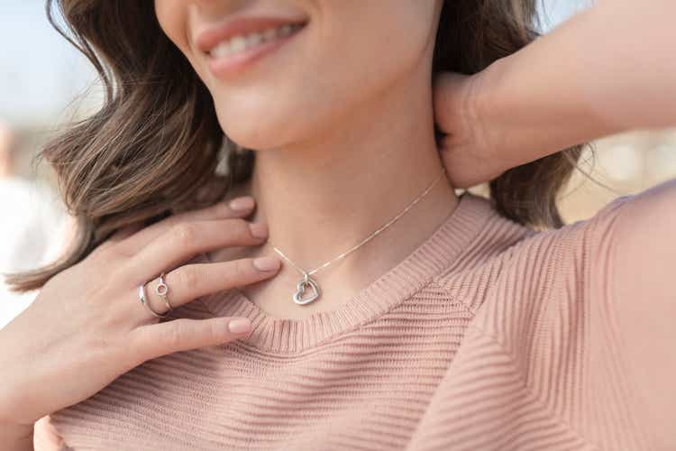 Close-up shot of a happy, beautiful woman putting on the silver necklace