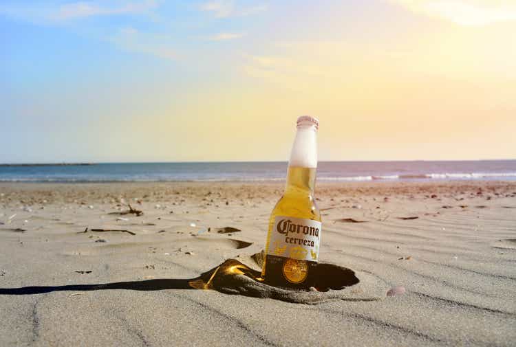 Corona Cerveza Beer Bottle on the beach near the sea. Cold beer on sunset background in the sand. Corona Extra Coronita Mexican Lager Bottle Glass.