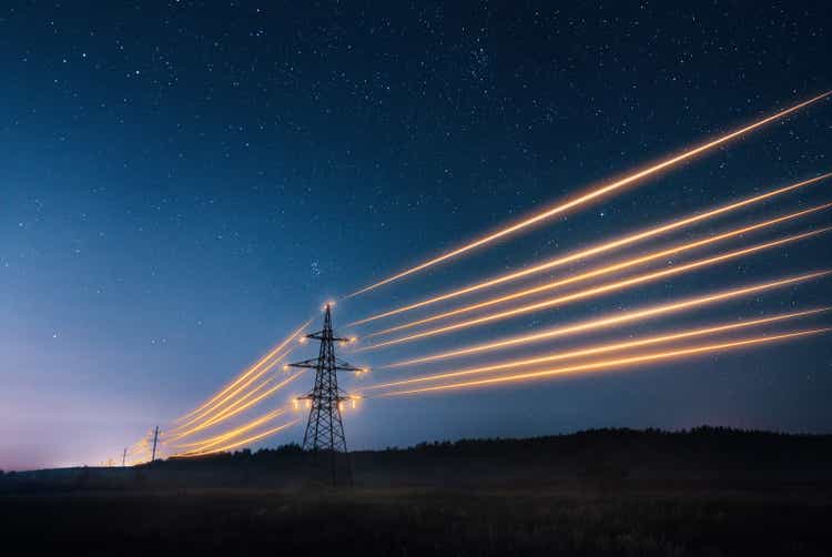 Electricity transmission towers with orange glowing wires against night sky.