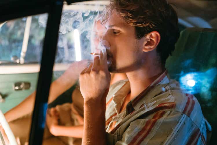 Young man smoking marijuana joint beside woman in car