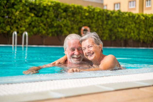 Couple of two happy seniors having fun and enjoying together in the swimming pool smiling and playing. Happy people enjoying summer outdoor in the water