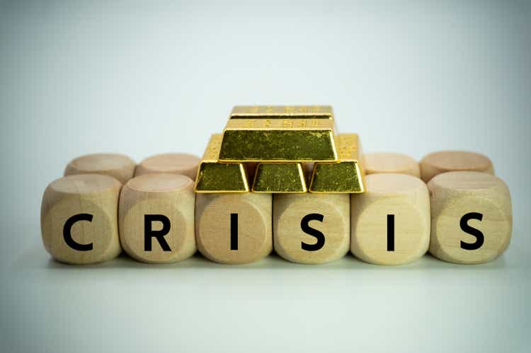 The crisis has raised the price of gold.international situation and finance theme.Money investment and risk control.safe haven asset.economic risk.A wooden sieve with word "Crisis" written on it holds a pile of gold nuggets.