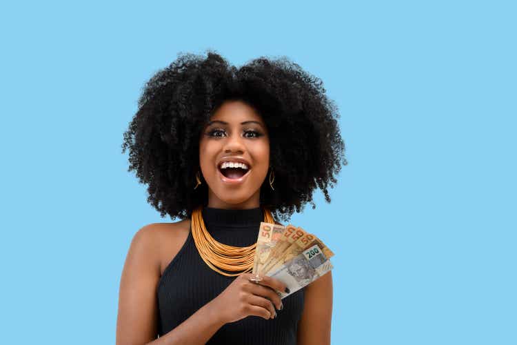 young black woman smiling holding brazilian money bills, positively surprised, space for text, person, advertising concept