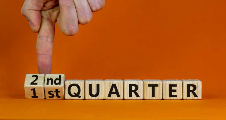 From 1st to 2nd quater symbol. Businessman turns cubes and changes words "1st quater" to "2nd quater". Beautiful orange table, orange background. Business, happy 2nd quater concept, copy space.