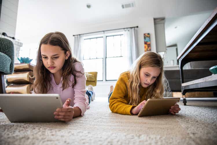 Tween sisters using digital tablets on living room floor