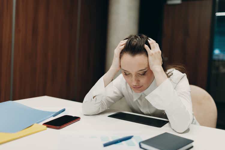 Sad businesswoman sit and hold head with his hands at office table. Business woman headache in crisis and depression after covid-19 pandemia concept