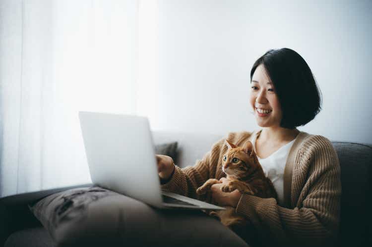 Cheerful young Asian woman browsing the internet with her cat at home during the pandemic time