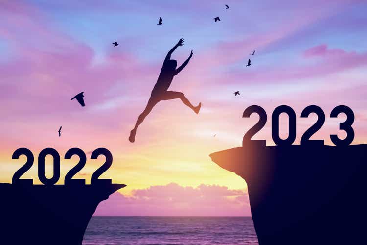 Silhouette man jumping between cliff with number 2022 to 2023 and birds flying at top of mountain. Freedom challenge and travel adventure holiday concept.