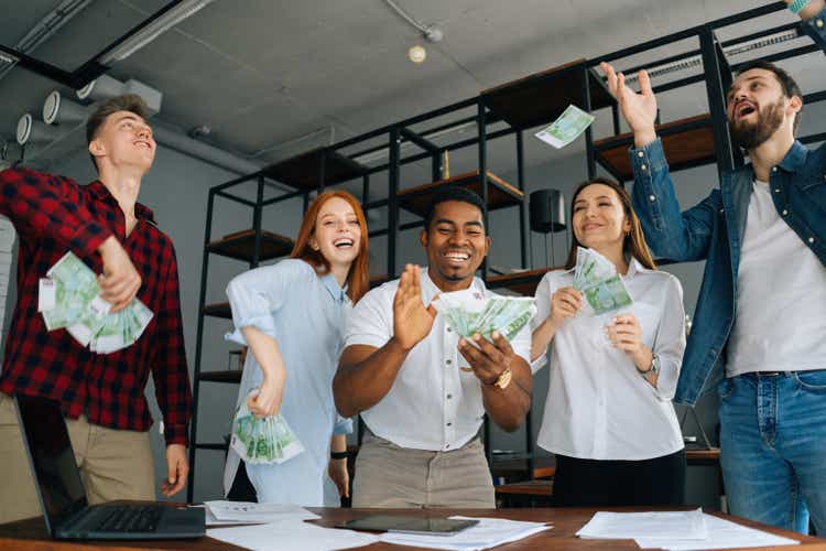 Low-angle shot of cheerful multi-ethnic employees celebrating victory and big profit