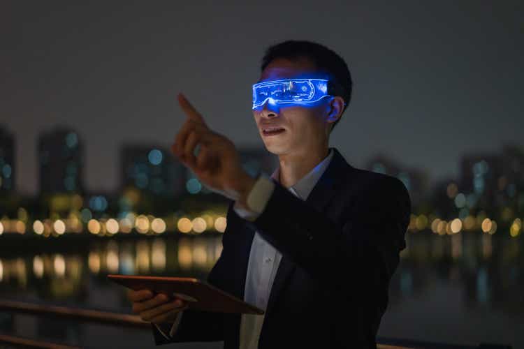Asian male office worker using augmented reality glasses outdoors to experience metaverse game at night