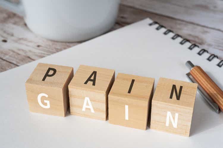 Wooden blocks with "PAIN" and "GAIN" text of concept, a pen, a notebook, and a cup.