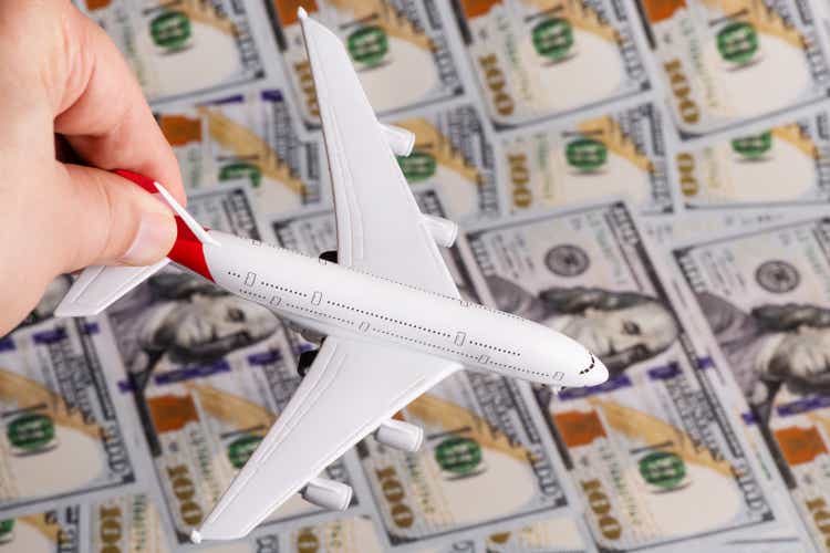 A symbolic passenger plane in the hand of a man and a banknote of 100 American dollars