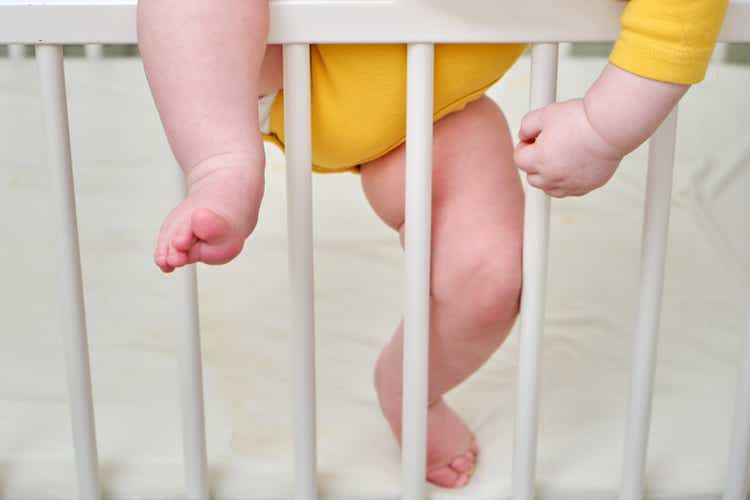 Toddler baby climbs the crib railing, legs close-up. Protect children from home, kids safety