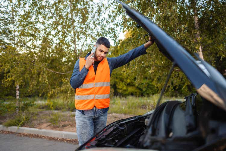 Young man in reflective vest calling roadside assistance after car breakdown