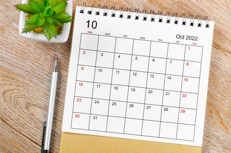 October 2022 desk calendar with pen on wooden table.
