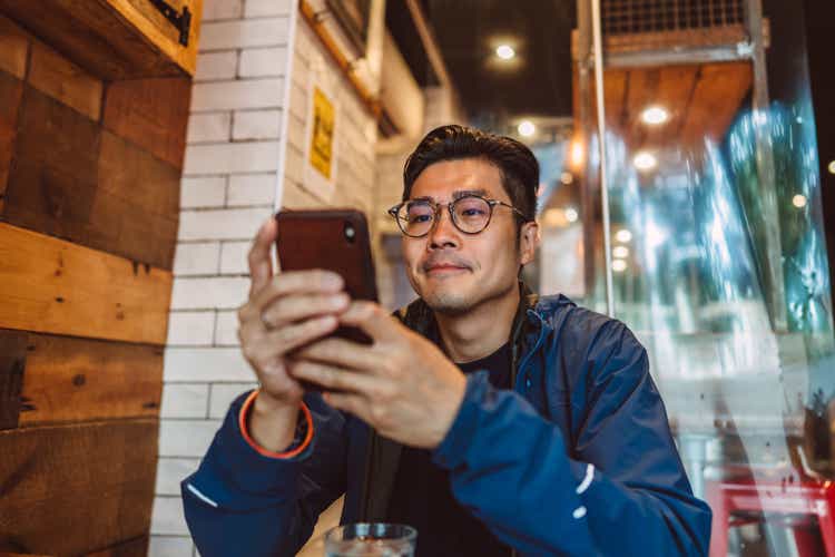 Young handsome Asian man making order from the digital menu on smartphone in restaurant