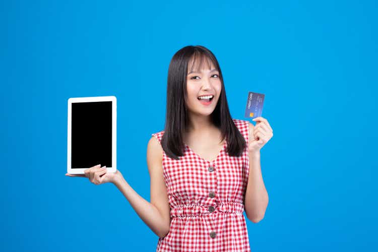 Portrait Asian happy young girl smiling cheerful and showing plastic credit card while holding mobile phone isolated on blue background