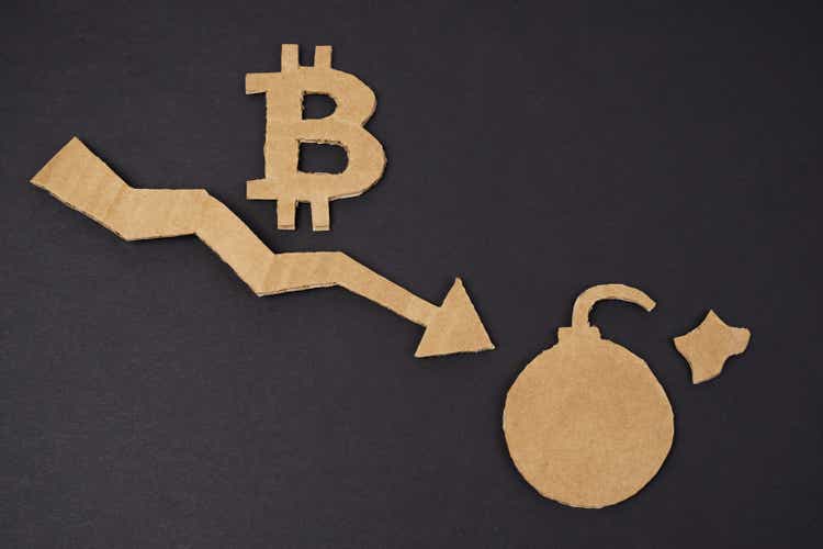 Concept of economic crisis. On a black surface, a graph with a down arrow, a bitcoin symbol and a bomb.