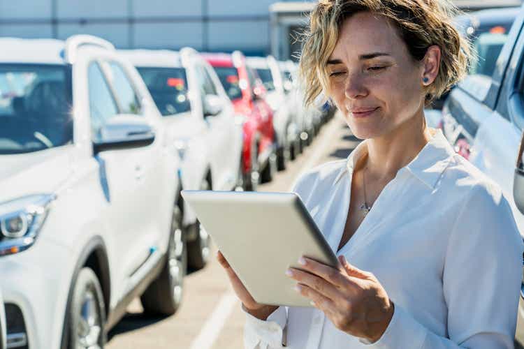 Saleswoman taking inventory at car dealership