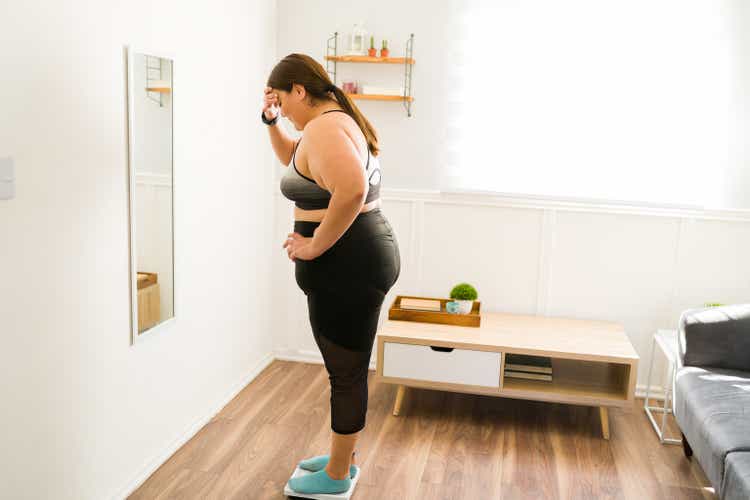 Stressed overweight woman using the weighing scale