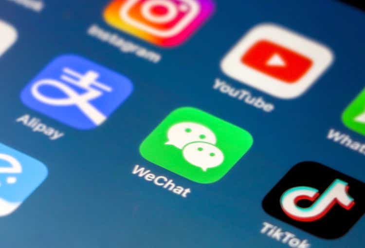WeChat Application Icon in focus on iPhone smartphone screen, other apps (Tik Tok, Alipay, Instagram etc) out of focus on blue gradient background wallpaper