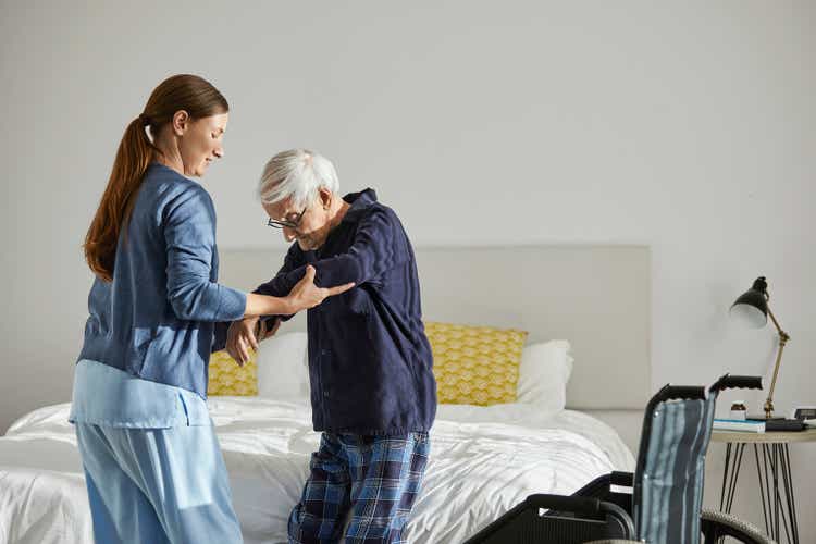 Female caregiver supporting senior man in standing