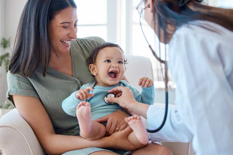 Shot of a baby sitting on her mother"s lap while being examined by a doctor