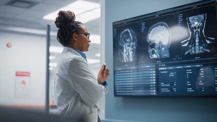 Medical Science Hospital: Confident Black Female Neurologist, Neuroscientist, Neurosurgeon, Looks at TV Screen with MRI Scan with Brain Images, Thinks about Sick Patient Treatment Method. Saving Lives