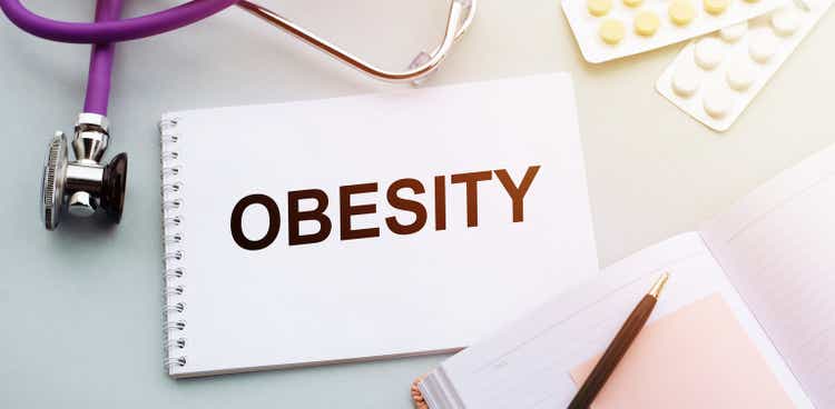 Stethoscope, pills and notebook with OBESITY word on medical desk.