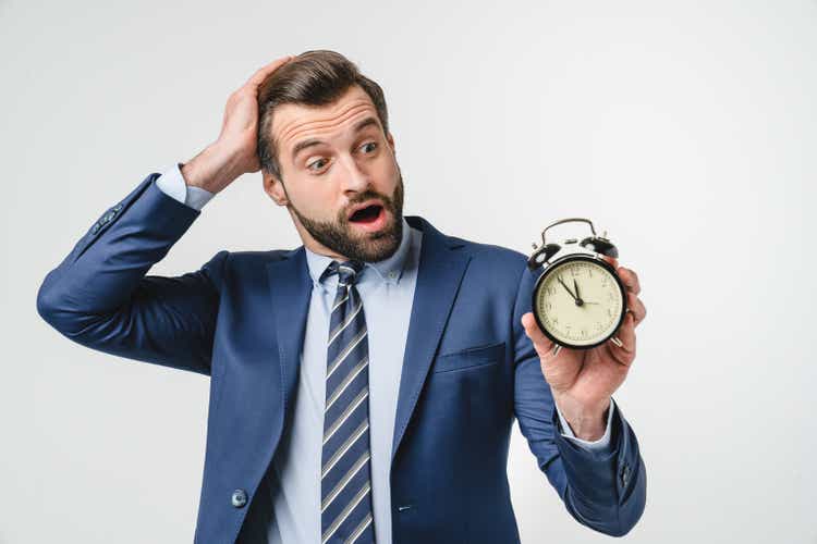 Confused shocked caucasian young businessman ceo manager freelancer teacher holding alarm clock for deadline, being late, high time for sale discount offer isolated in white background