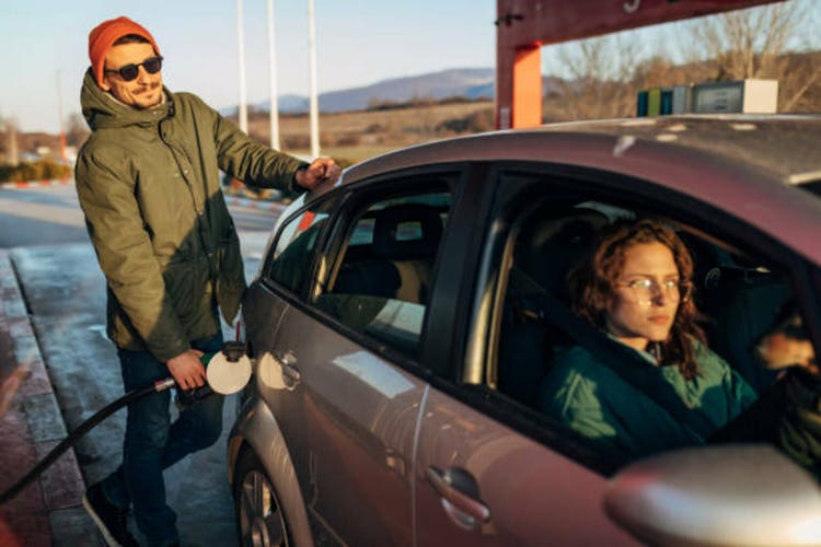 A smiling millennial man refueling a car at a natural gas station