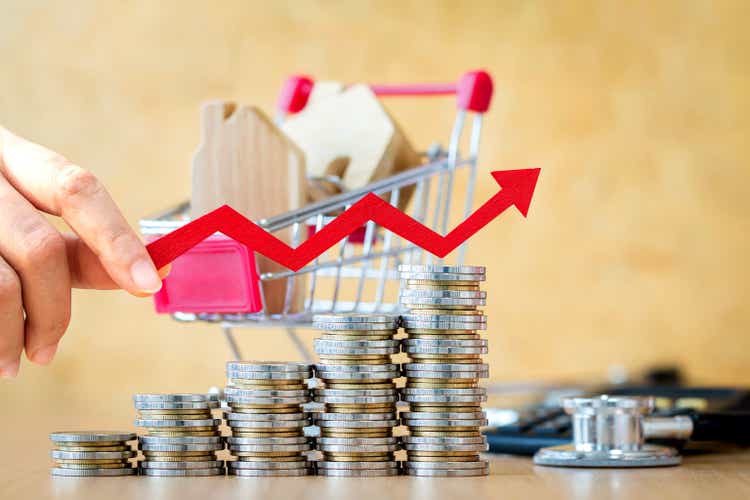 Woman hand hold a red arrow graph with growing value and shopping cart and home model put in inside in the office, Buy or sell a house and real estate for working capital concept.
