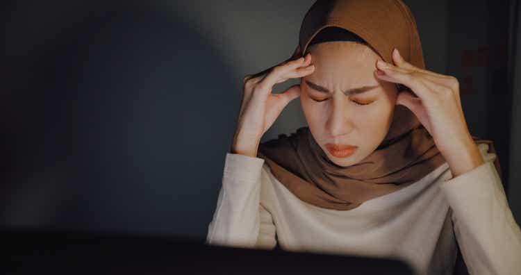 Close up of Frustrated young Asian muslim businesswoman wearing hijab working on a laptop and using tablet sitting at desk in office at home.