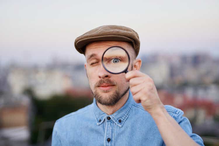 Man in peaked cap looking at camera using magnifying glass