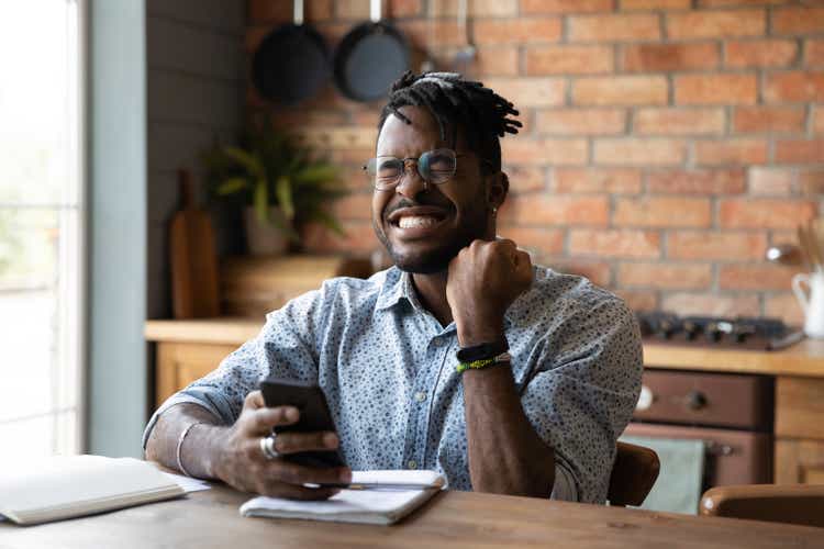 Overjoyed millennial African guy reading message on smartphone