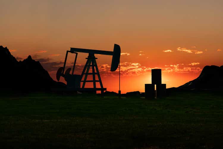 Silhouette of a oil pump and oil barrels in the desert steppe between mountains during sunset.