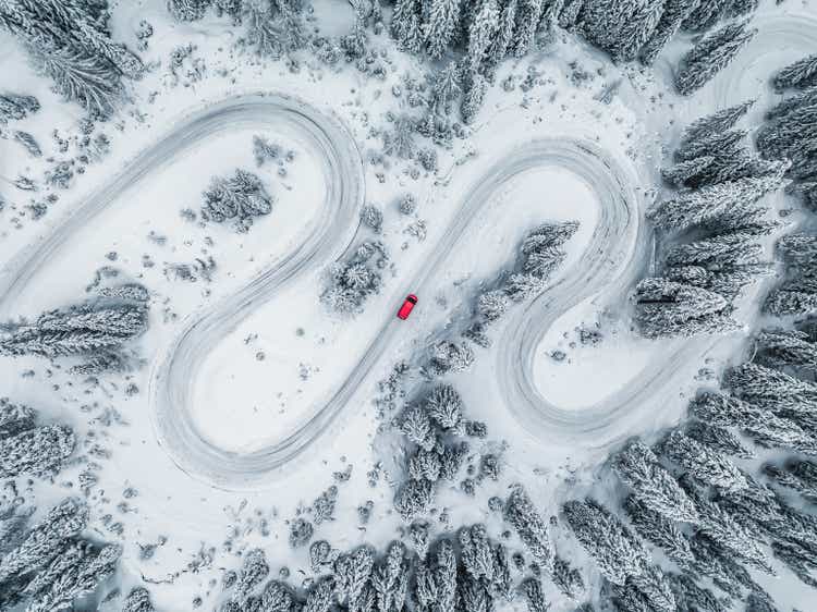 Camper van driving on a winding road through a snow covered forest seen from directly above, Dolomites, Italy