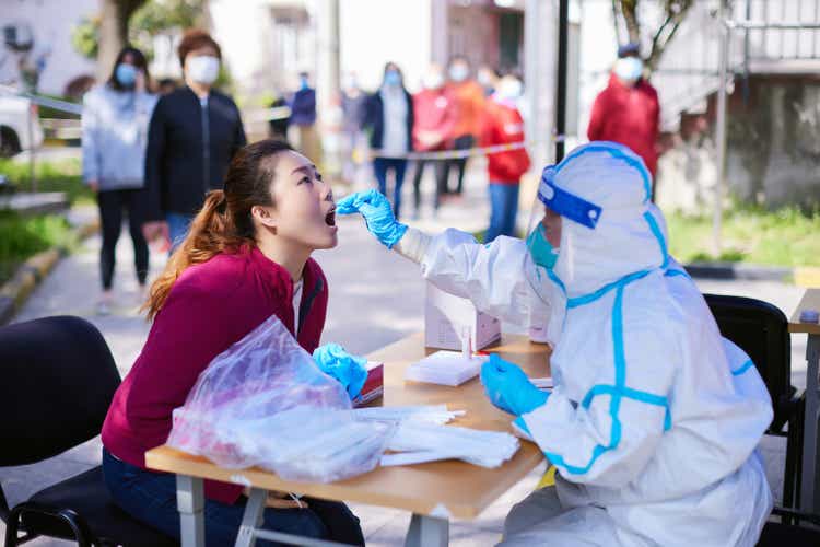 In April 2022, a medical worker wearing protective clothing conducts nucleic acid testing and sampling for a woman in Shanghai, China.