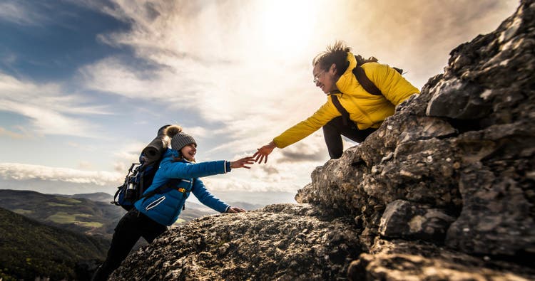 People helping each other hike up a mountain at sunrise - Giving helping hand and teamwork concept